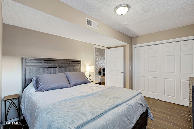 bedroom featuring a textured ceiling, visible vents, a closet, and wood finish floors