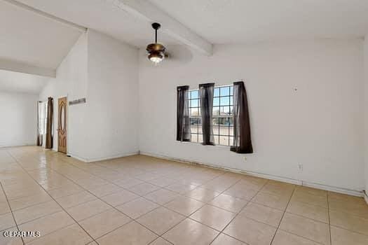 empty room featuring vaulted ceiling with beams, light tile patterned floors, and baseboards