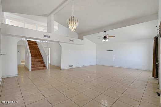 unfurnished living room with high vaulted ceiling, ceiling fan with notable chandelier, visible vents, stairs, and beam ceiling