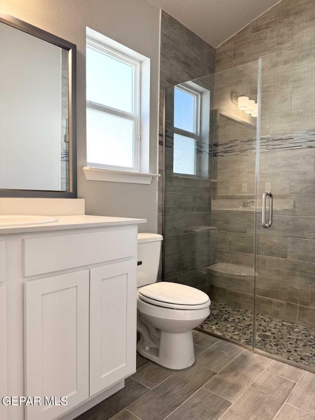 full bath with a stall shower, toilet, lofted ceiling, wood tiled floor, and vanity