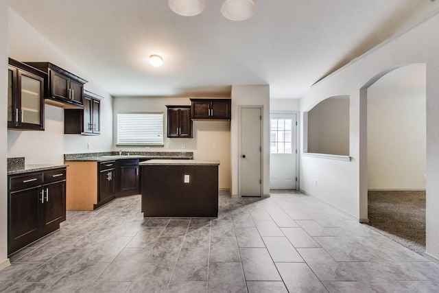 kitchen featuring a center island, arched walkways, stone countertops, dark brown cabinetry, and a sink