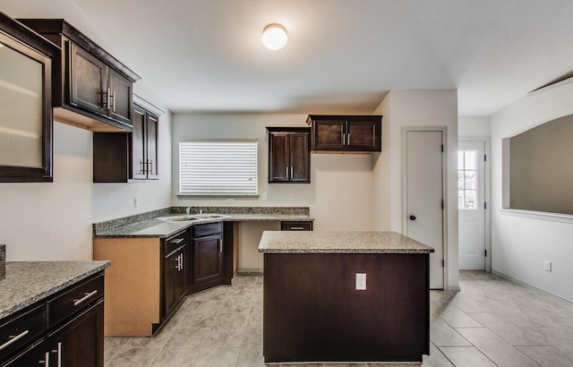 kitchen featuring a sink, dark brown cabinets, light stone counters, and a kitchen island