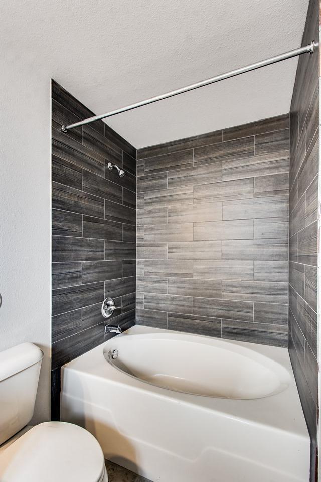 bathroom with a textured ceiling, bathing tub / shower combination, and toilet