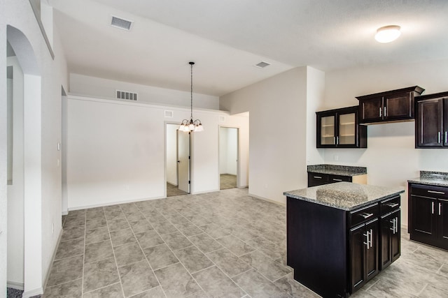 kitchen featuring light stone counters, a center island, visible vents, and dark brown cabinets