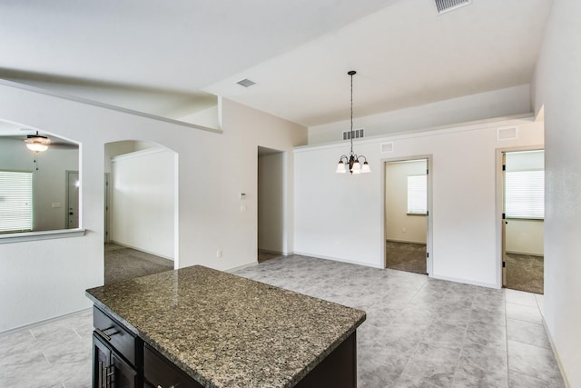 kitchen featuring visible vents, arched walkways, dark stone counters, a kitchen island, and decorative light fixtures