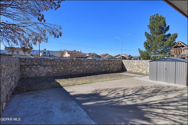 view of yard with a storage shed, a fenced backyard, a residential view, an outbuilding, and a patio area