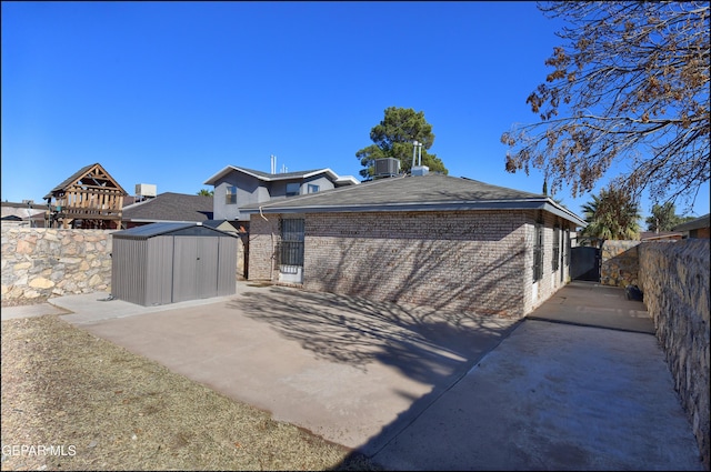 exterior space with a storage shed, central AC unit, a fenced backyard, an outdoor structure, and brick siding