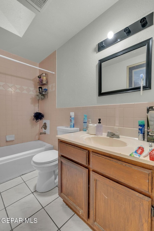 full bathroom featuring a skylight, tile walls, toilet, vanity, and  shower combination