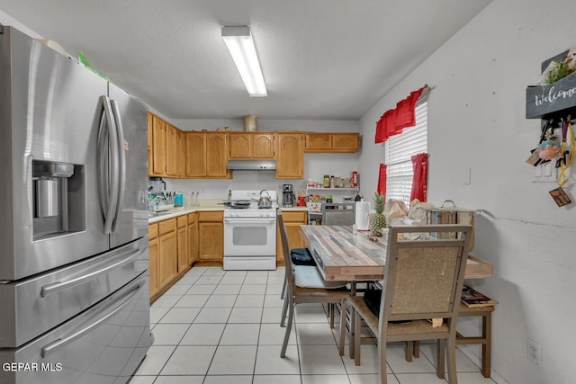 kitchen featuring white range with gas cooktop, stainless steel fridge with ice dispenser, light countertops, under cabinet range hood, and light tile patterned flooring