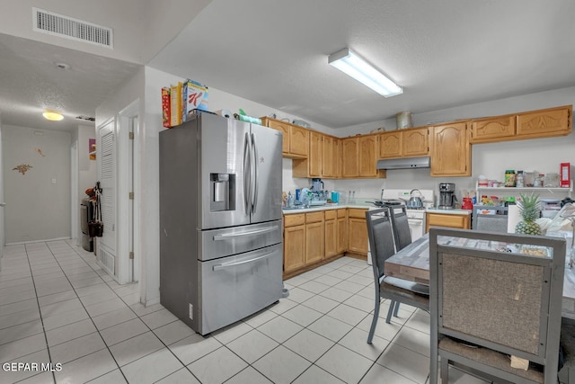 kitchen with light tile patterned floors, light countertops, visible vents, stainless steel fridge, and under cabinet range hood