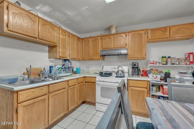 kitchen featuring light tile patterned floors, white gas stove, under cabinet range hood, a sink, and light countertops