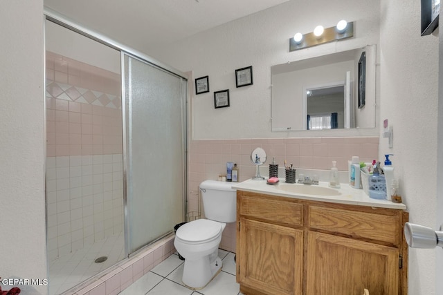 bathroom with a stall shower, toilet, tile patterned floors, vanity, and tile walls