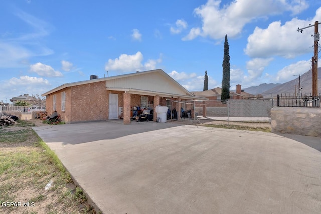 view of side of property featuring fence, a mountain view, a patio, and brick siding