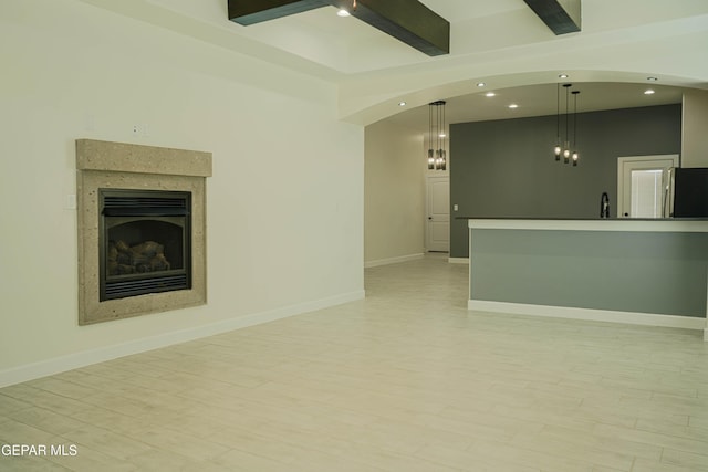 unfurnished living room with a sink, light wood-style flooring, a fireplace, and beamed ceiling