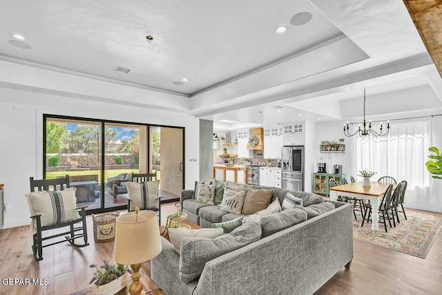 living area with recessed lighting, a raised ceiling, light wood-style flooring, and a notable chandelier