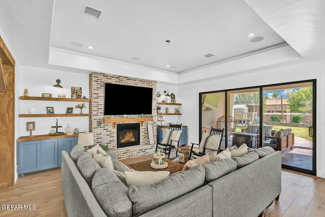 living area featuring light wood-style floors, a fireplace, visible vents, and a raised ceiling