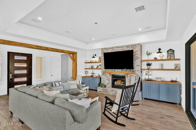 living room with light wood-style floors, a tray ceiling, and visible vents