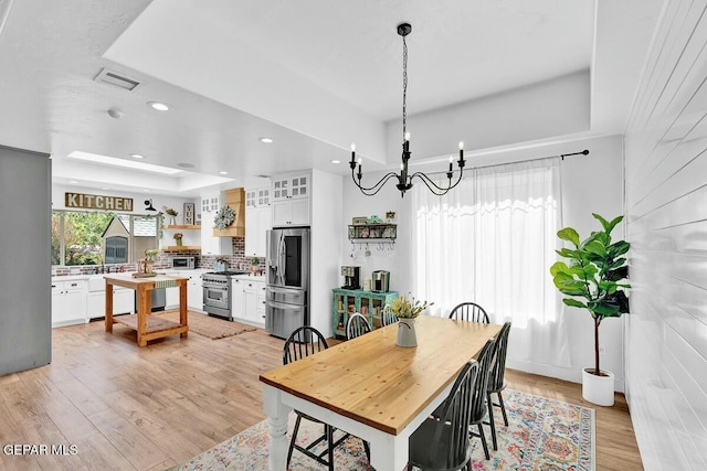 dining area with light wood-style flooring, visible vents, a raised ceiling, and recessed lighting