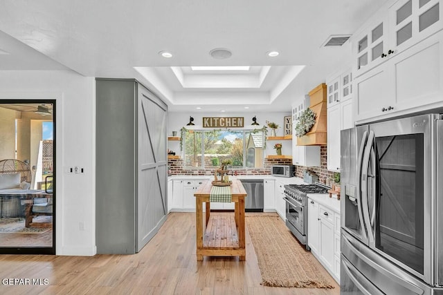 kitchen featuring premium range hood, stainless steel appliances, a tray ceiling, and open shelves