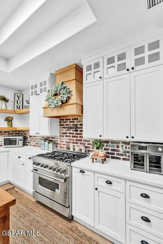 kitchen with white cabinets, light countertops, high end stainless steel range oven, and open shelves