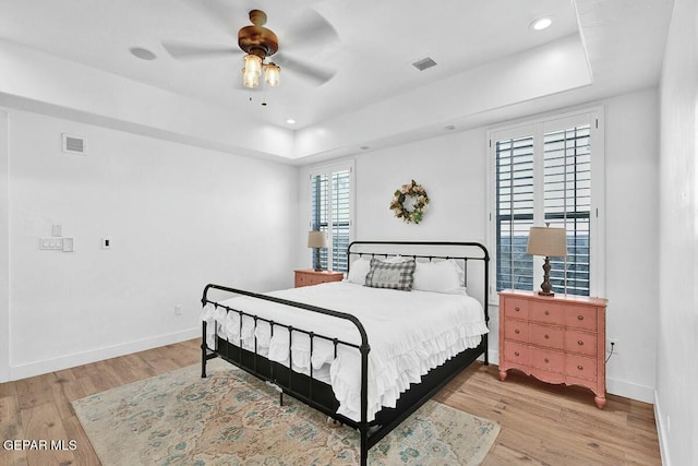 bedroom featuring light wood-style flooring, visible vents, baseboards, and a raised ceiling