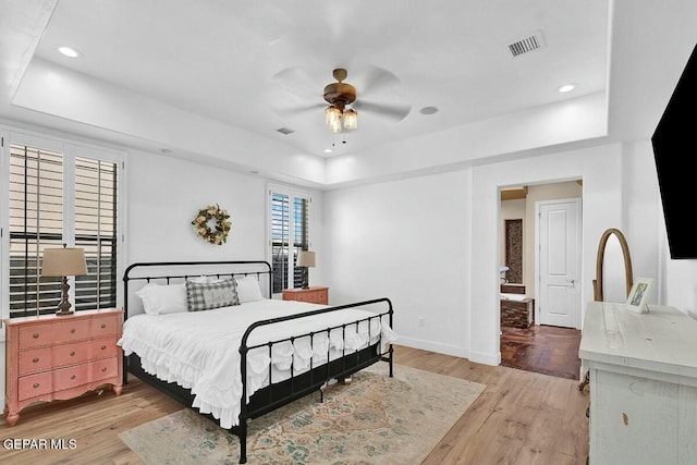 bedroom featuring light wood-style flooring, visible vents, a raised ceiling, and baseboards