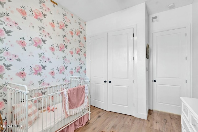 bedroom featuring a crib, wallpapered walls, visible vents, light wood-style flooring, and a closet