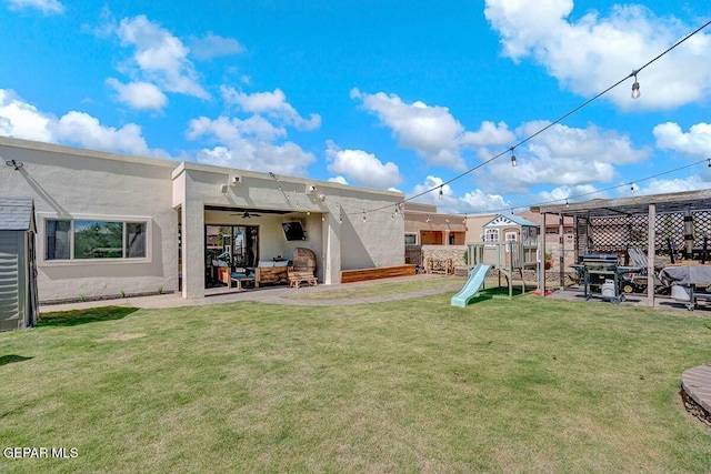 rear view of property with a playground, stucco siding, a lawn, a patio area, and fence