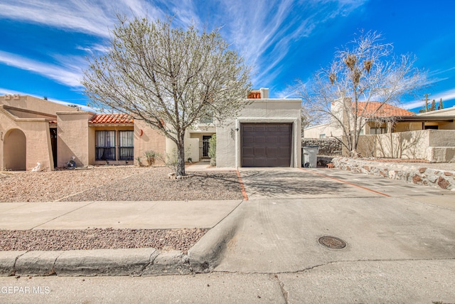 adobe home with driveway, a tiled roof, an attached garage, fence, and stucco siding