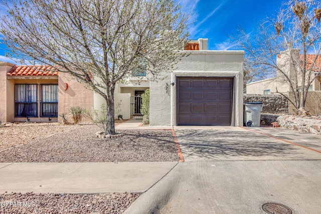 pueblo-style home with concrete driveway, a tile roof, an attached garage, and stucco siding