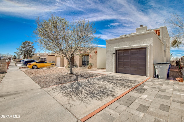 pueblo revival-style home featuring a garage, concrete driveway, a chimney, and stucco siding