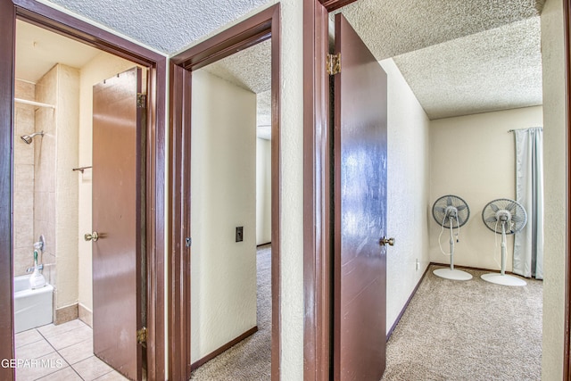 hallway featuring light tile patterned floors, baseboards, a textured ceiling, and light colored carpet