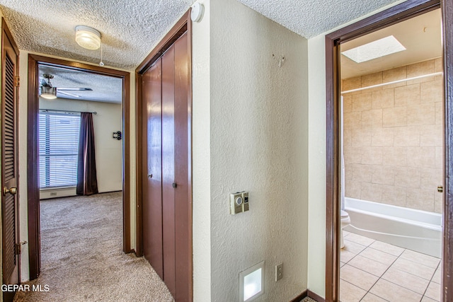 hall featuring a textured ceiling, a textured wall, light tile patterned floors, and light colored carpet