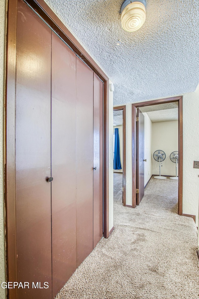 hallway featuring light carpet, a textured wall, and a textured ceiling