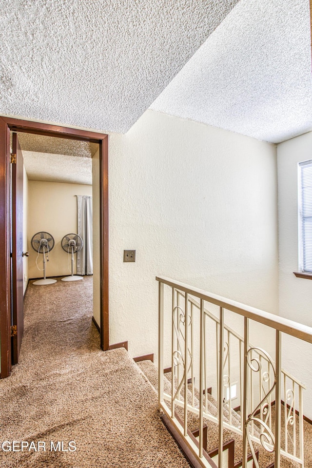 corridor featuring carpet flooring, a textured wall, and a textured ceiling