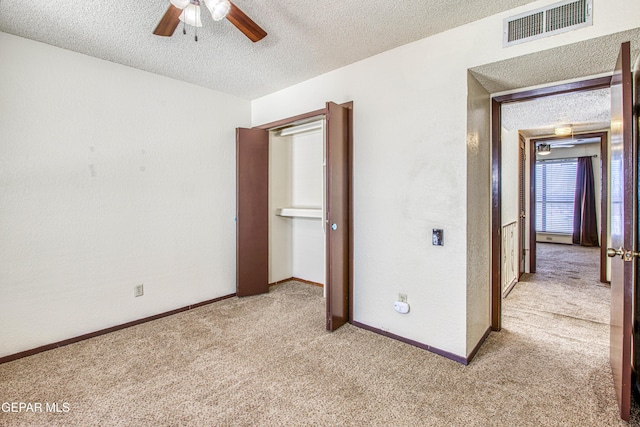 unfurnished bedroom with baseboards, visible vents, a ceiling fan, light colored carpet, and a textured ceiling