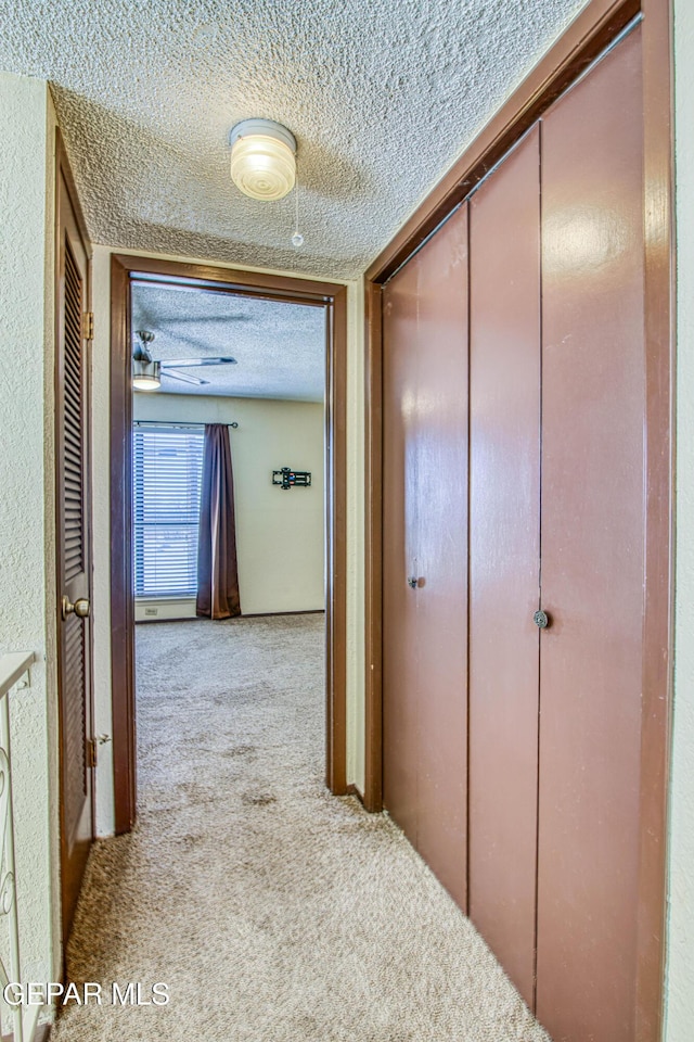 hallway with light carpet and a textured ceiling