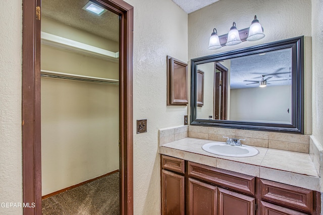 bathroom featuring a walk in closet, a textured wall, a textured ceiling, and vanity