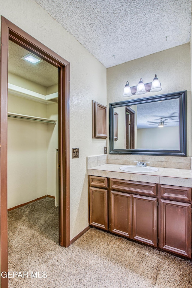 bathroom with a textured wall, a walk in closet, a textured ceiling, and vanity