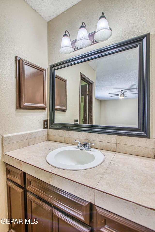 bathroom with a textured ceiling, ceiling fan, a textured wall, and vanity