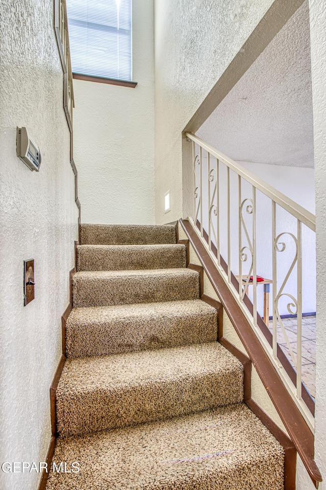 stairway featuring a textured ceiling and a textured wall