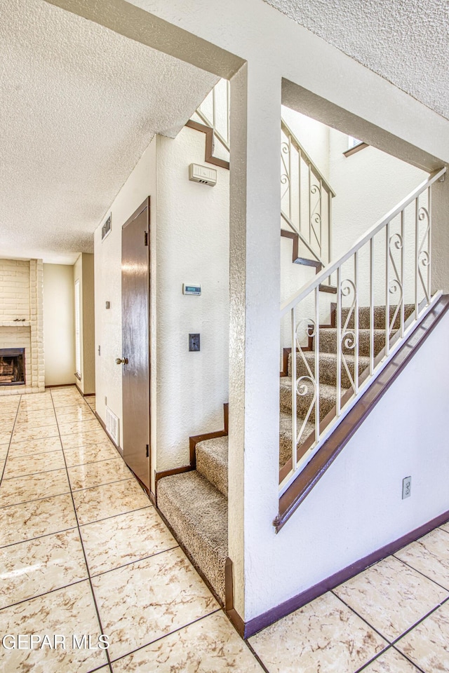 staircase with a brick fireplace, visible vents, baseboards, and a textured ceiling