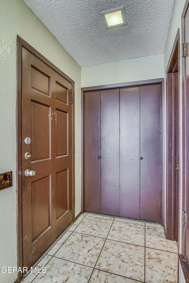 foyer featuring a textured wall, a textured ceiling, and light tile patterned flooring