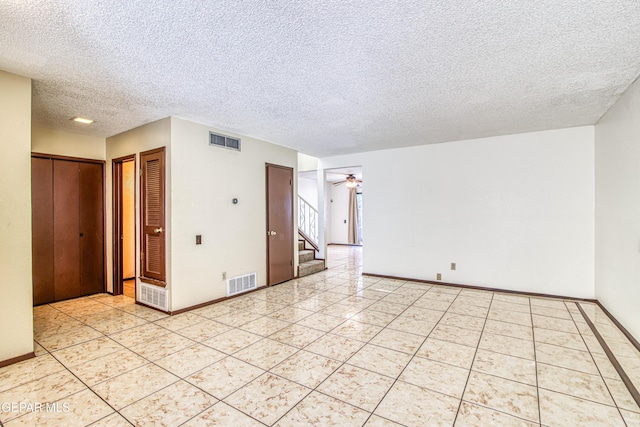 empty room with light tile patterned floors, ceiling fan, stairs, and visible vents