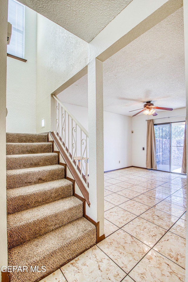 staircase with a ceiling fan, a textured ceiling, and baseboards