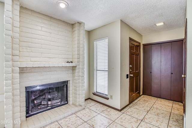 entryway featuring baseboards, a textured ceiling, light tile patterned flooring, and a brick fireplace