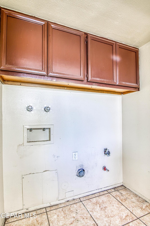 clothes washing area featuring gas dryer hookup, cabinet space, a textured ceiling, and light tile patterned flooring