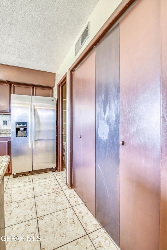 kitchen featuring stainless steel refrigerator with ice dispenser, light tile patterned floors, visible vents, light countertops, and a textured ceiling