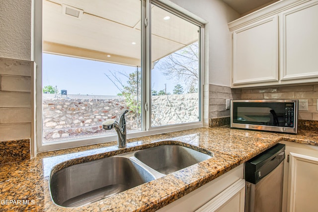 kitchen featuring a sink, stainless steel appliances, stone counters, backsplash, and white cabinets