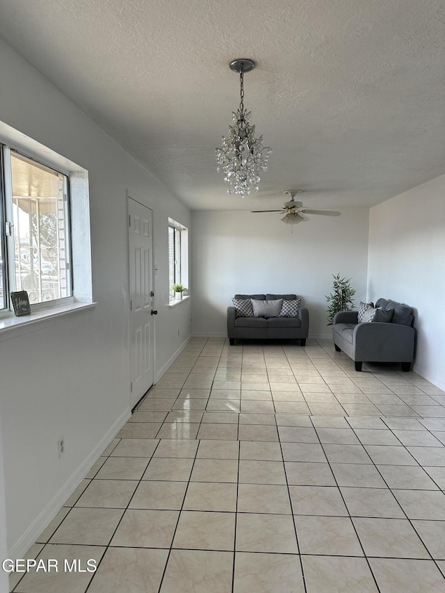 foyer entrance with ceiling fan with notable chandelier, a textured ceiling, baseboards, and light tile patterned floors